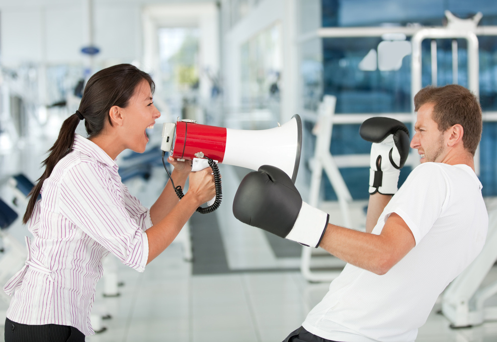 Tough female trainer yelling to a man with a megaphone while boxing